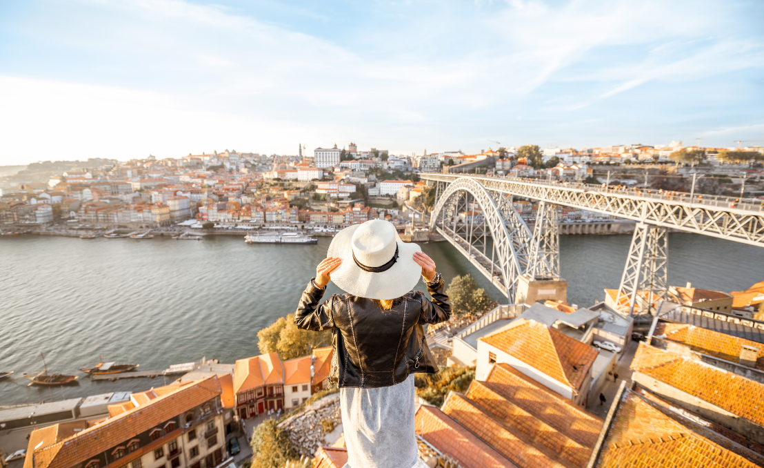 Panoramic view of Porto and the Douro River with Dom Luís I Bridge; a person in a hat looks out from a viewpoint.