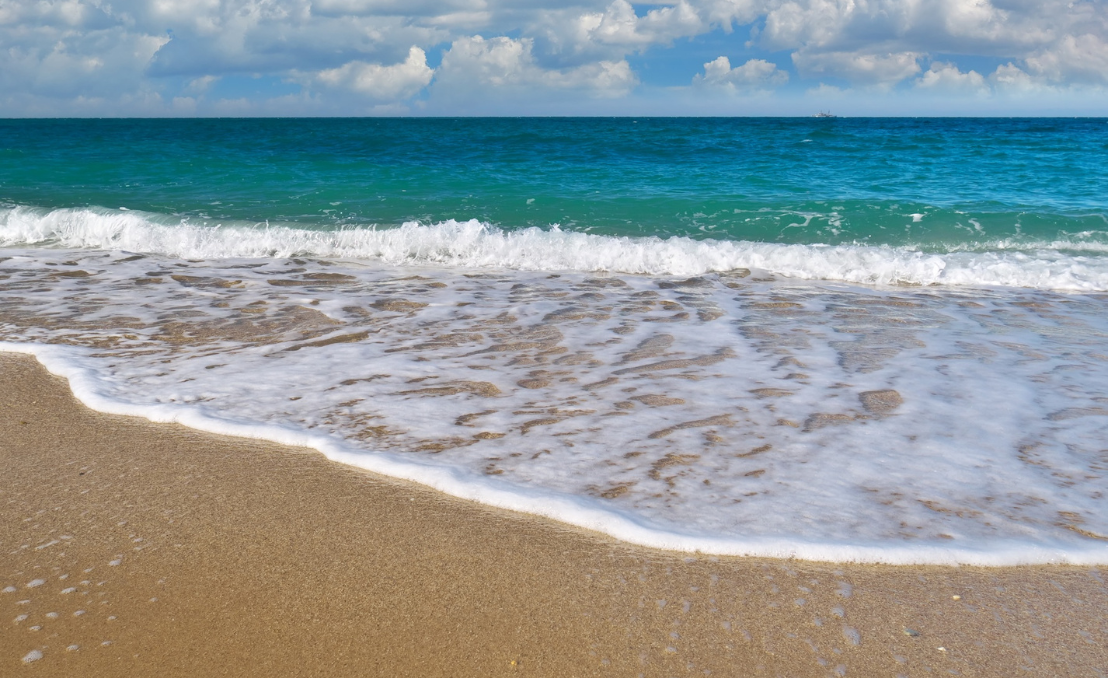 Ondas do mar a chegar à areia numa praia com céu azul