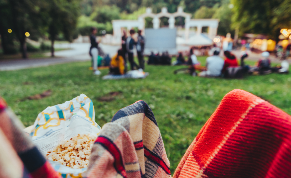 People sitting on grass watching an open-air cinema screening in a park at dusk