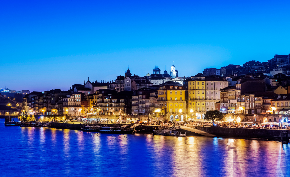 Vista noturna do Porto com o rio Douro e luzes da cidade refletidas na água
