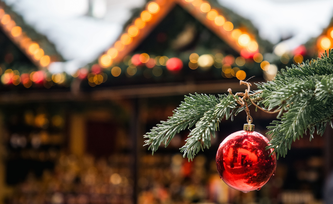 Red Christmas bauble with illuminated Christmas market stalls in the background
